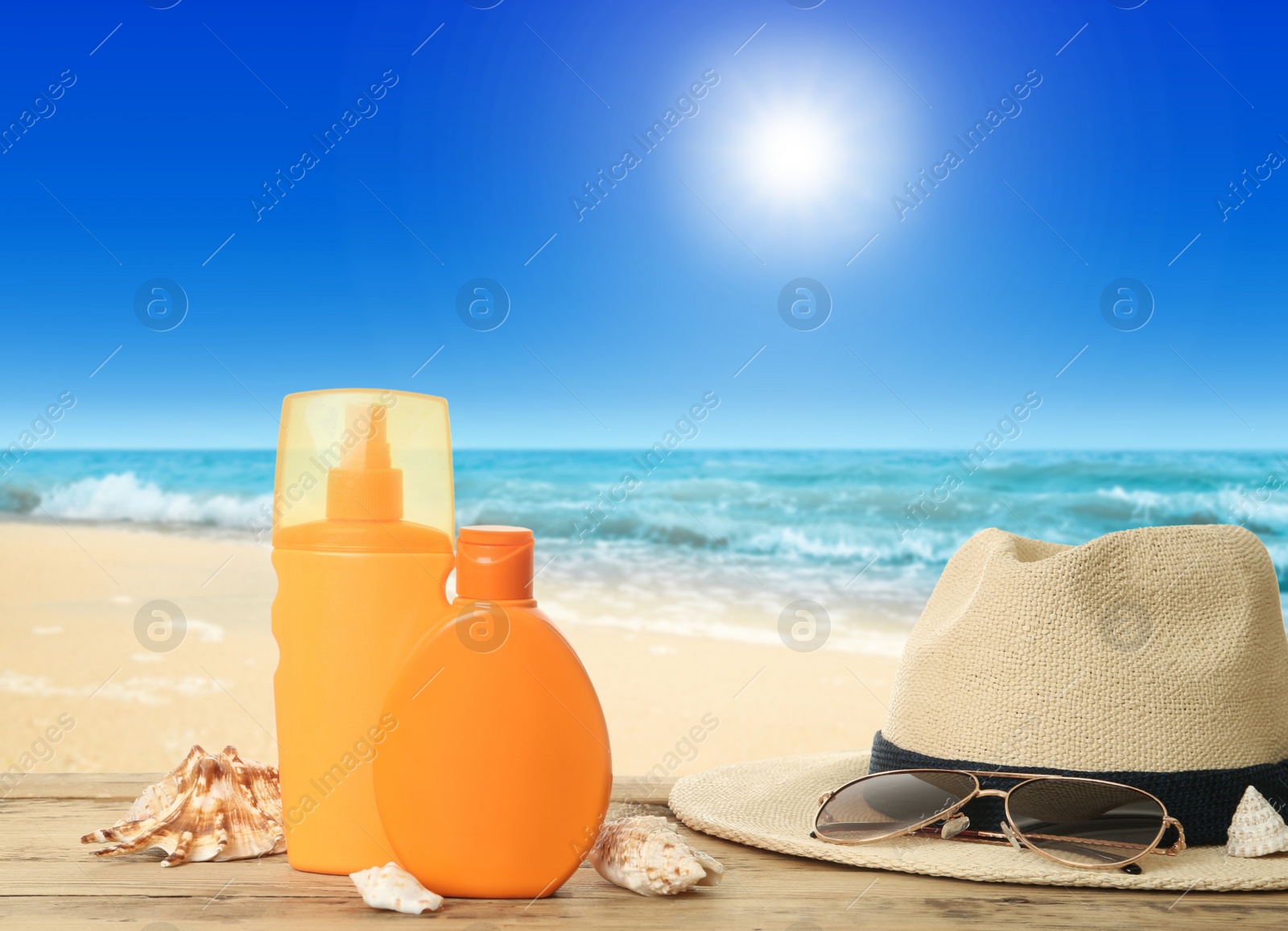 Image of Bottles of skin sun protection products and beach accessories on wooden table against seascape. Space for design