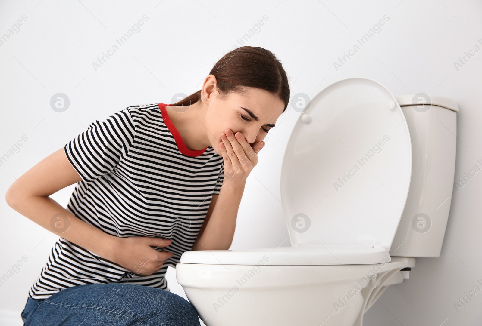 Photo of Young woman suffering from nausea at toilet bowl indoors