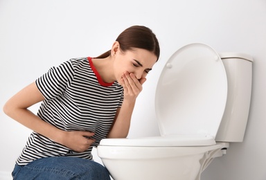Photo of Young woman suffering from nausea at toilet bowl indoors