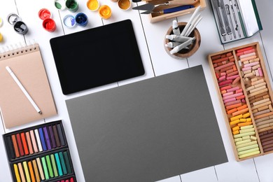 Photo of Blank sheet of paper, colorful chalk pastels, tablet and other drawing tools on white wooden table, flat lay. Modern artist's workplace