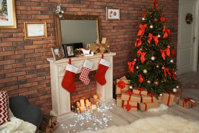 Photo of Beautiful Christmas tree and gifts near decorative fireplace with stockings indoors