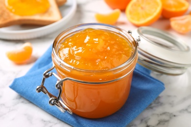 Photo of Tasty tangerine jam in glass jar on white marble table