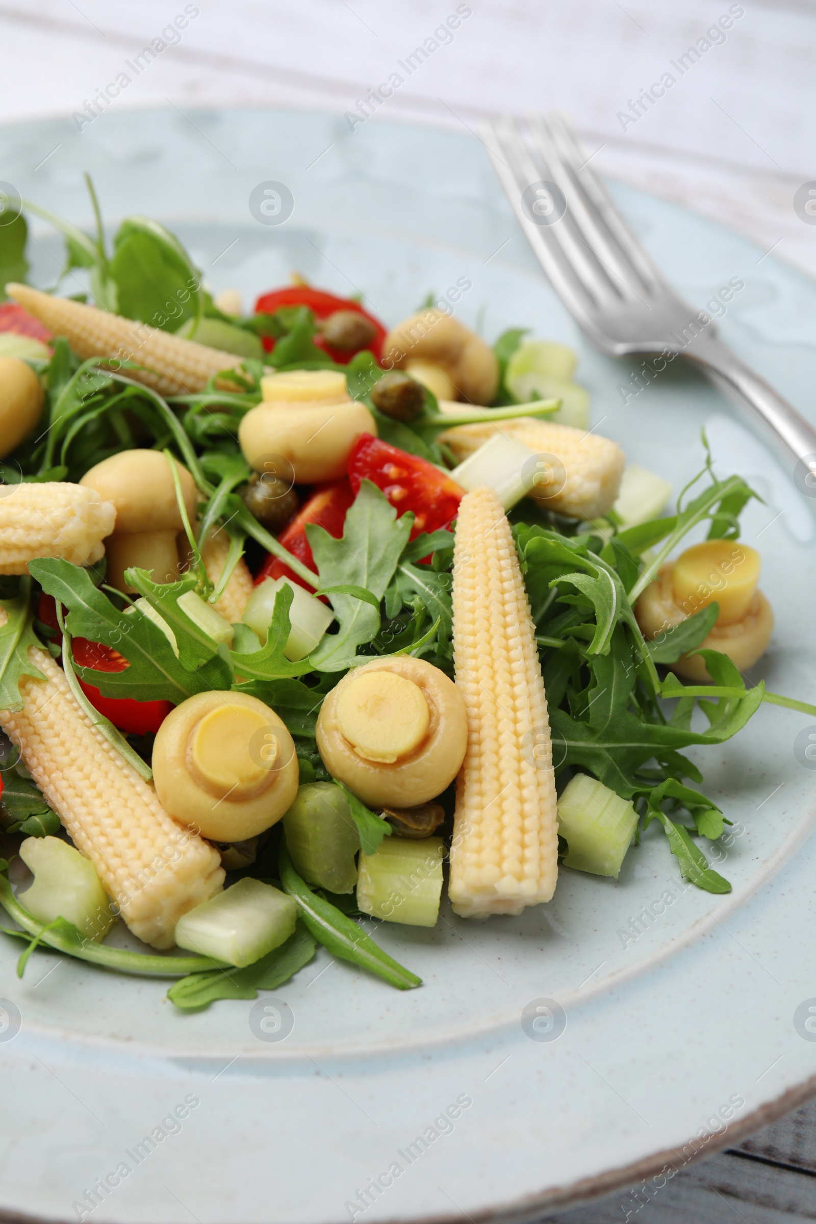 Photo of Tasty baby corn with vegetables, arugula and mushrooms on white wooden table, closeup