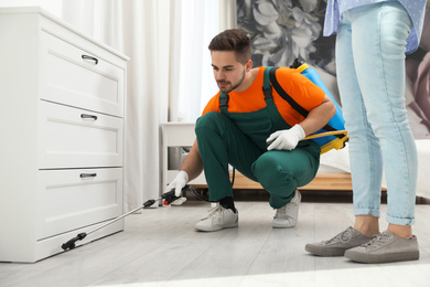Photo of Pest control worker spraying insecticide near chest of drawers indoors