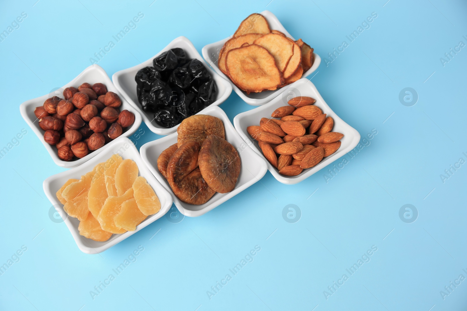 Photo of Bowls with dried fruits and nuts on light blue background, space for text