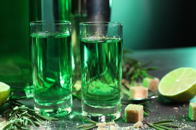 Photo of Absinthe in shot glasses, brown sugar, rosemary and lime on gray table, closeup. Alcoholic drink