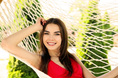 Photo of Young woman relaxing in hammock outdoors on warm summer day