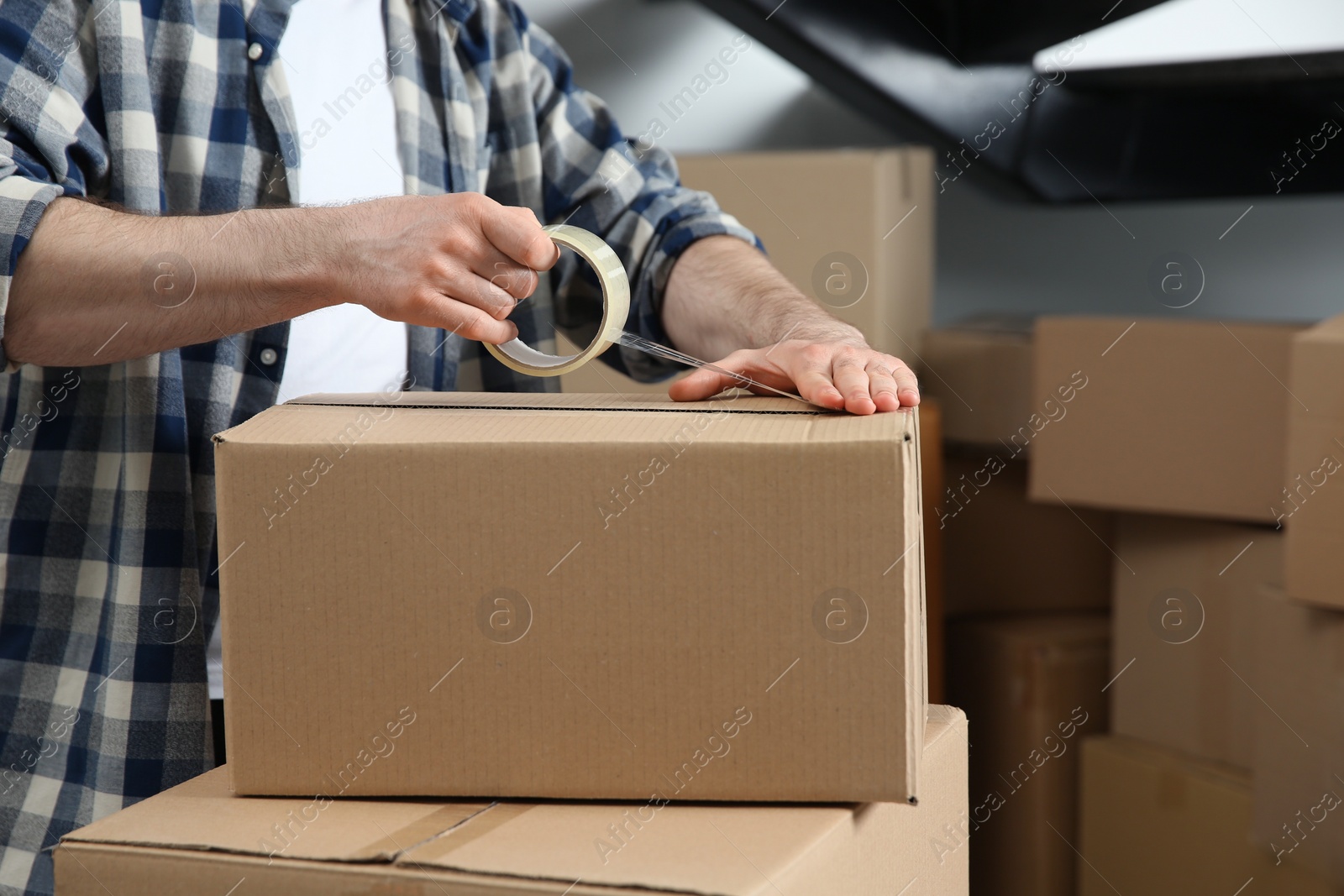 Photo of Man taping cardboard box indoors, closeup. Moving day