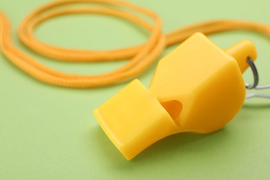 Photo of One yellow whistle with cord on light green background, closeup