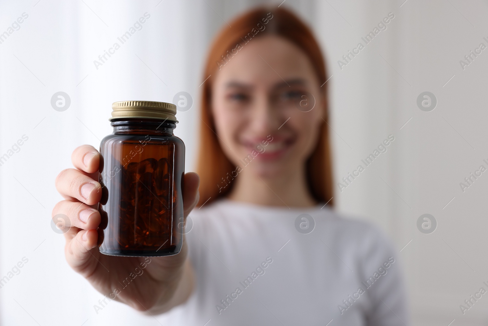 Photo of Beautiful young woman with jar of vitamin pills at home, selective focus