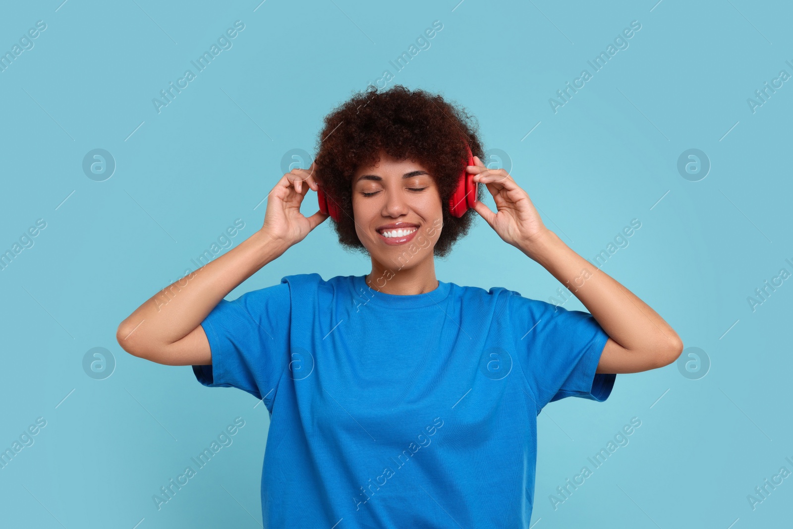 Photo of Beautiful young woman in headphones enjoying music on light blue background