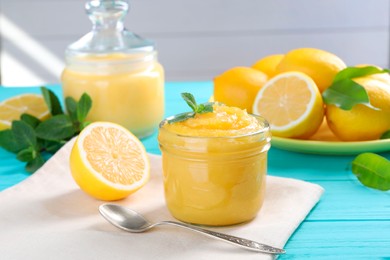 Delicious lemon curd in glass jar, fresh citrus fruits, mint and spoon on light blue wooden table