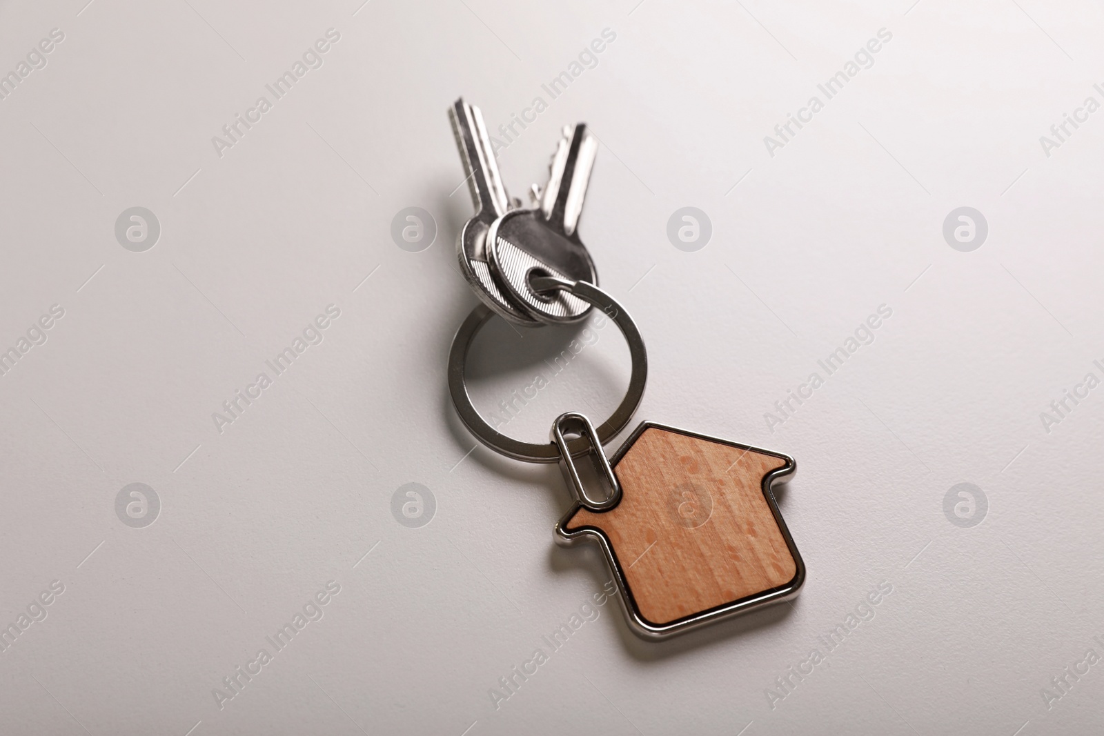 Photo of Keys with trinket in shape of house on white background, above view. Real estate agent services