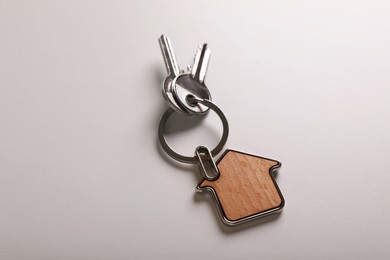 Keys with trinket in shape of house on white background, above view. Real estate agent services