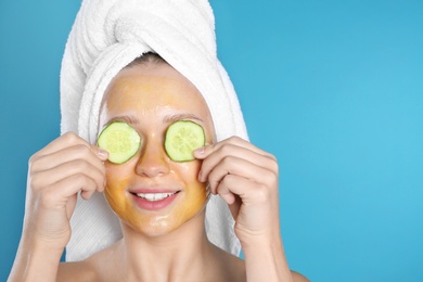 Photo of Beautiful woman holding cucumber slices near her face with natural mask against color background. Space for text