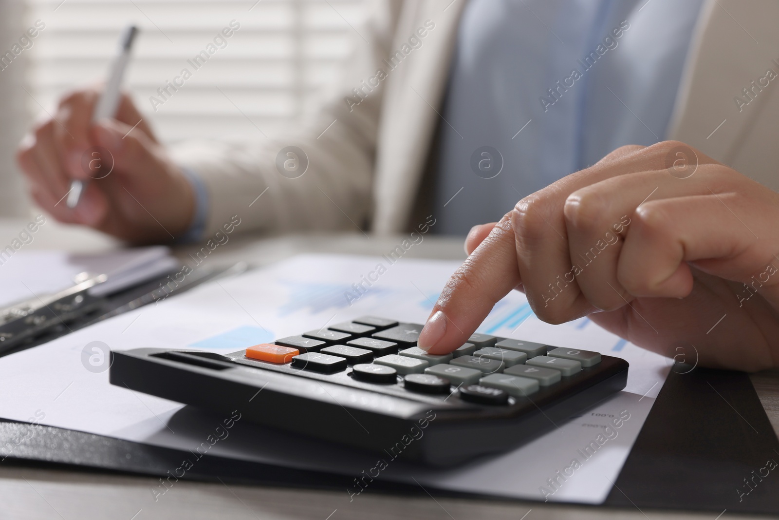 Photo of Woman using calculator at table in office, closeup