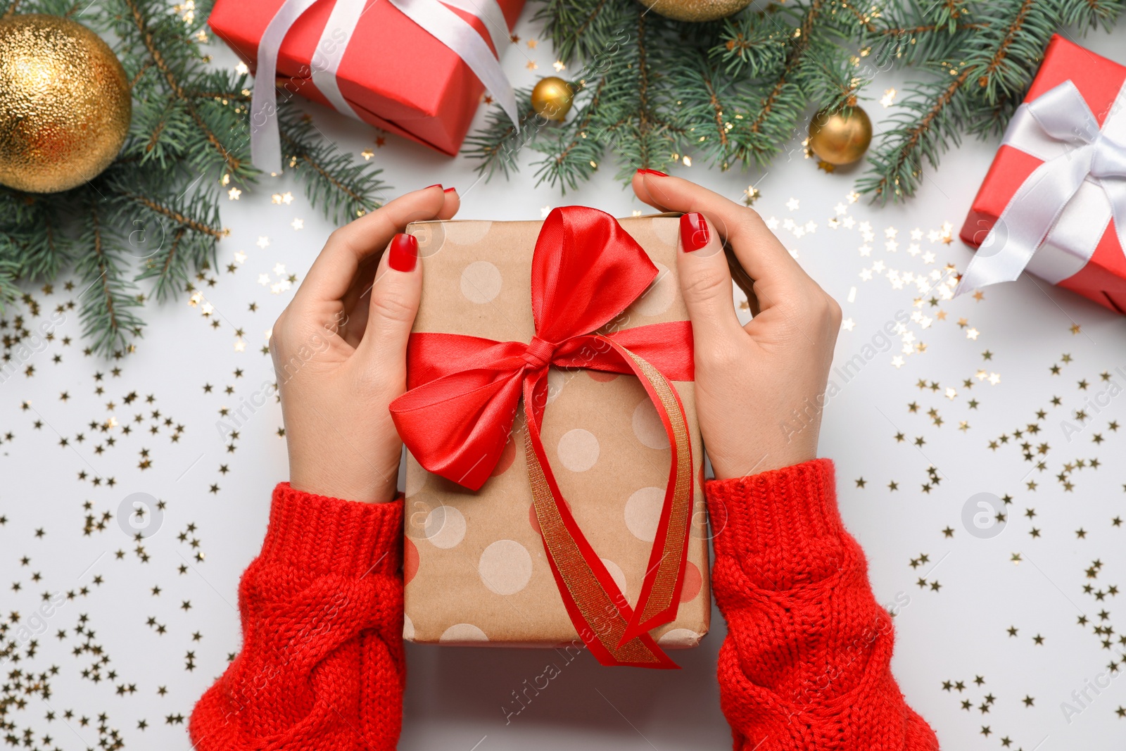 Photo of Woman holding gift box near fir tree branches with Christmas decor on white background, top view