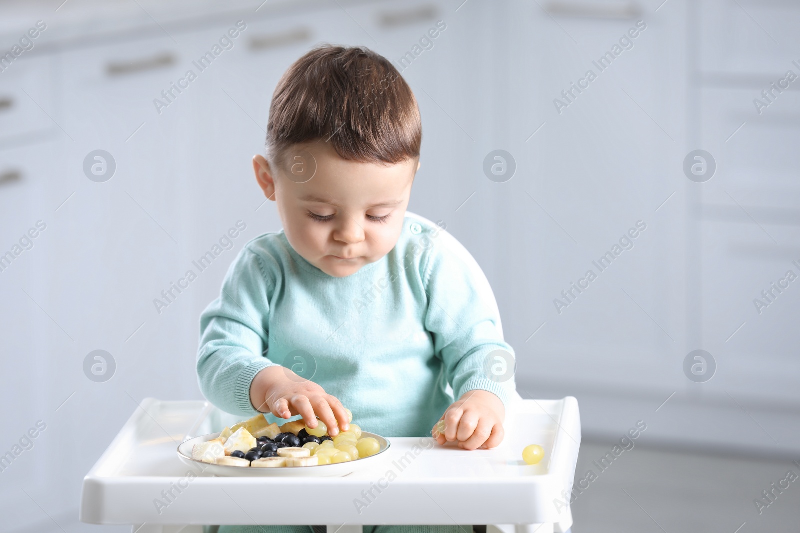 Photo of Cute little baby eating healthy food in high chair at home. Space for text