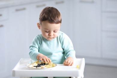 Photo of Cute little baby eating healthy food in high chair at home. Space for text