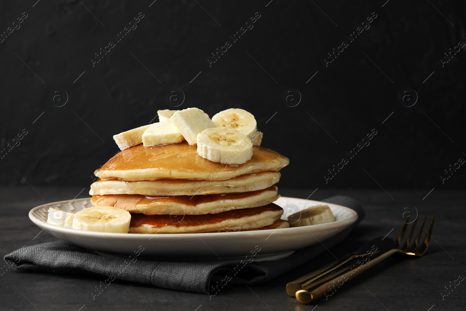 Photo of Delicious pancakes with bananas, butter and honey on dark table. Space for text