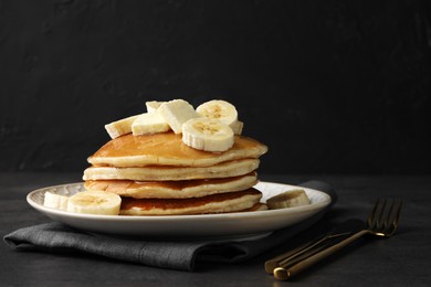 Photo of Delicious pancakes with bananas, butter and honey on dark table. Space for text