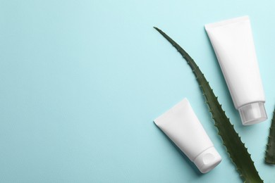 Tubes of hand cream and aloe on turquoise background, flat lay. Space for text