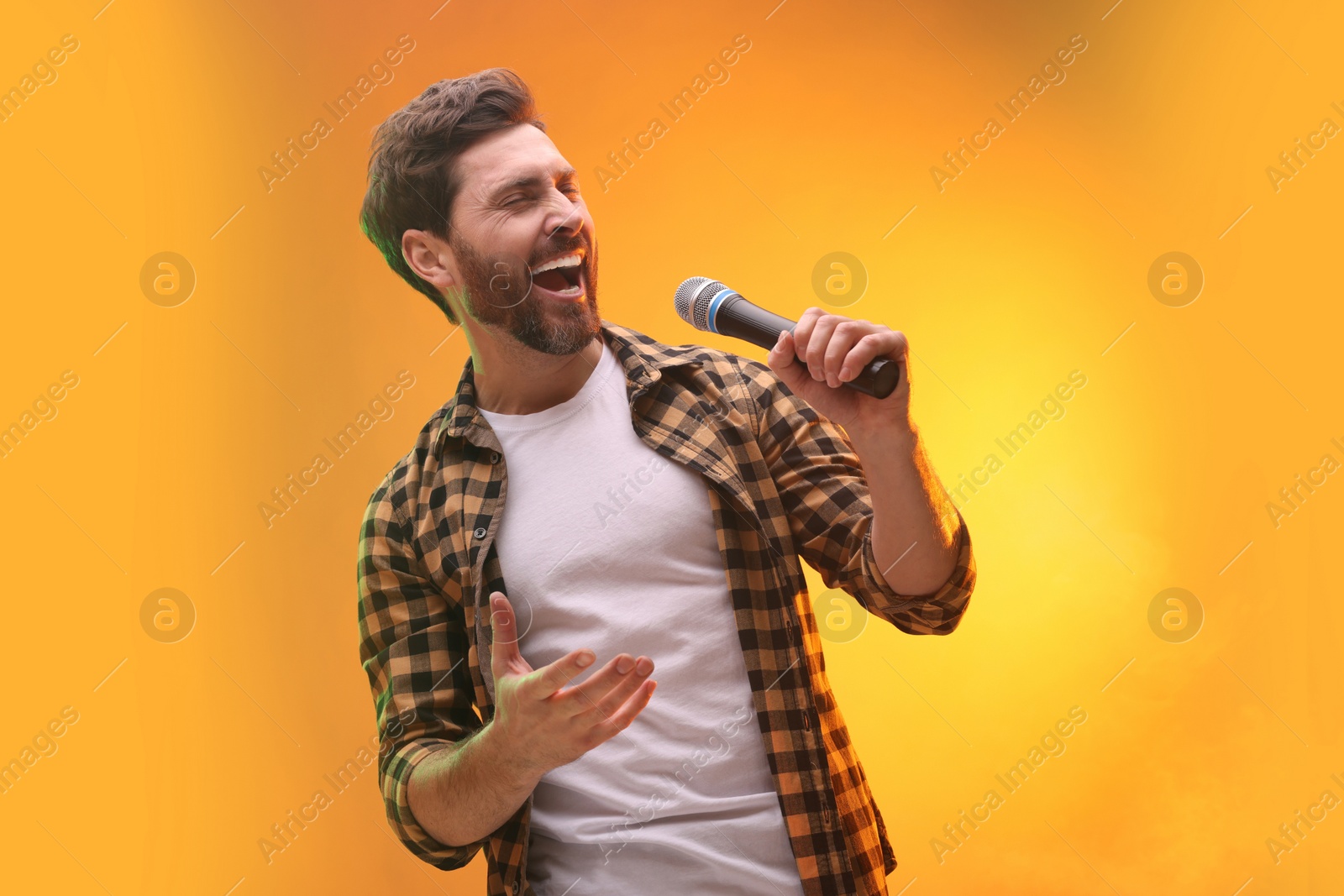 Photo of Handsome man with microphone singing on golden background