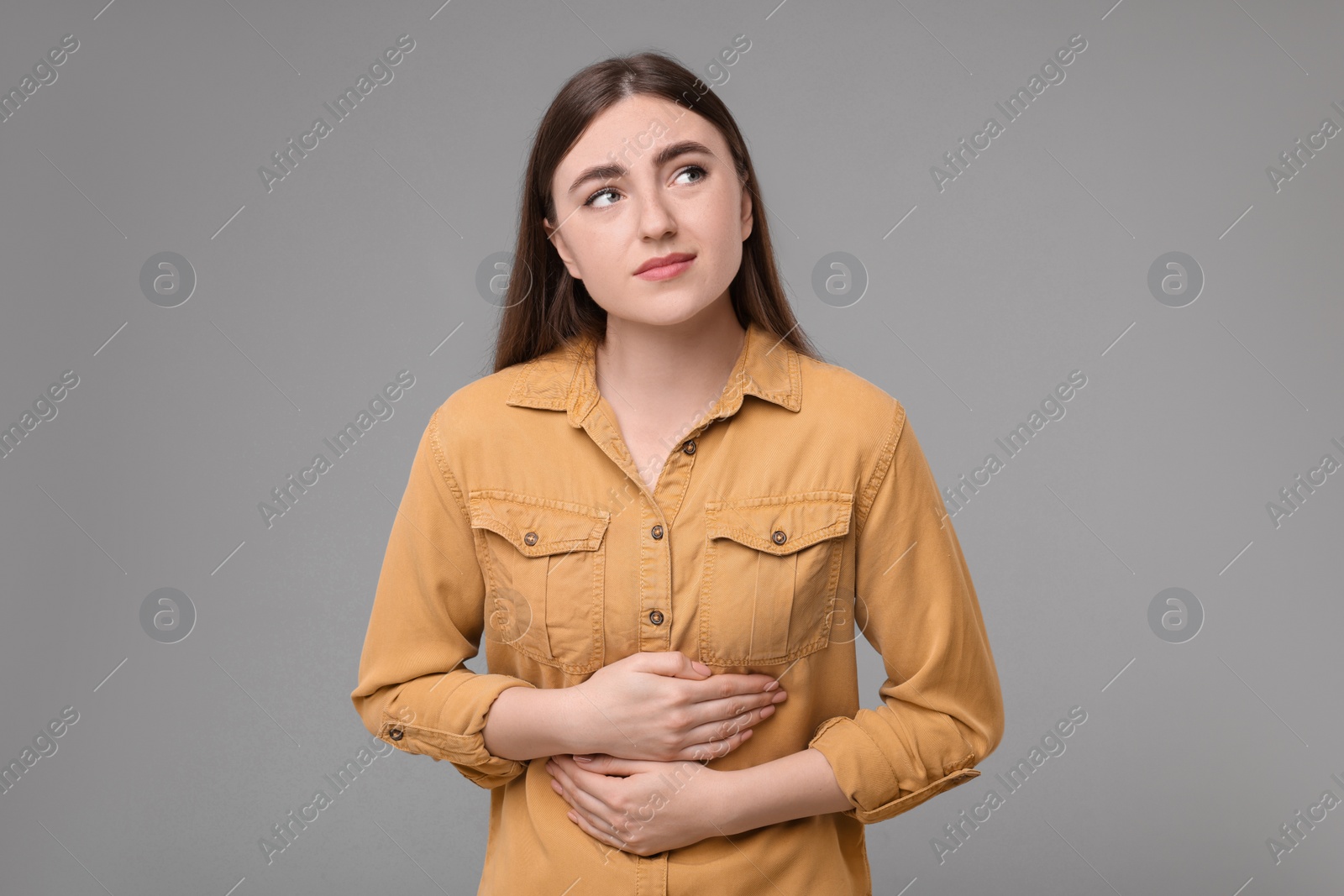 Photo of Young woman suffering from stomach pain on grey background