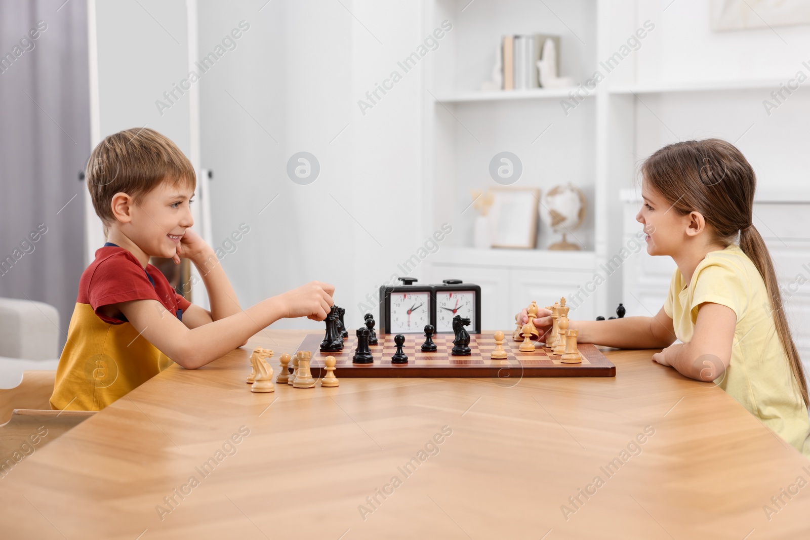 Photo of Cute children playing chess at table in room