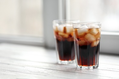 Glasses of cola with ice near window, space for text