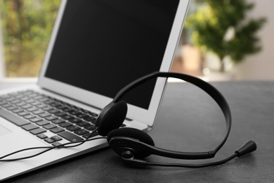 Photo of Modern laptop and headset on table. Technical support concept