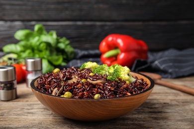 Photo of Bowl with delicious cooked brown rice on wooden table