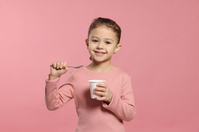 Girl with tasty yogurt on pink background