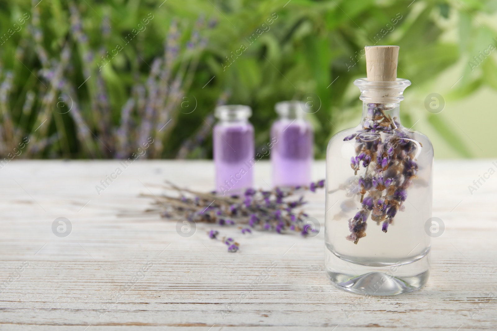 Photo of Bottle with natural herbal oil and lavender flowers on table against blurred background. Space for text