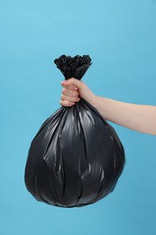 Photo of Woman holding plastic bag full of garbage on light blue background, closeup