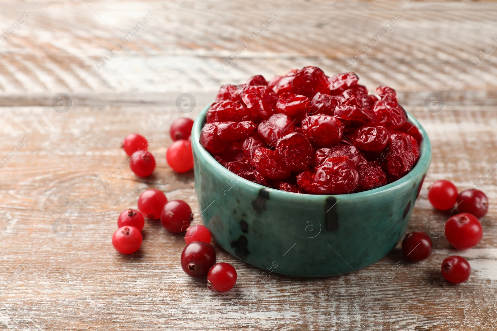 Photo of Tasty dried cranberries in bowl and fresh ones on rustic wooden table, closeup. Space for text