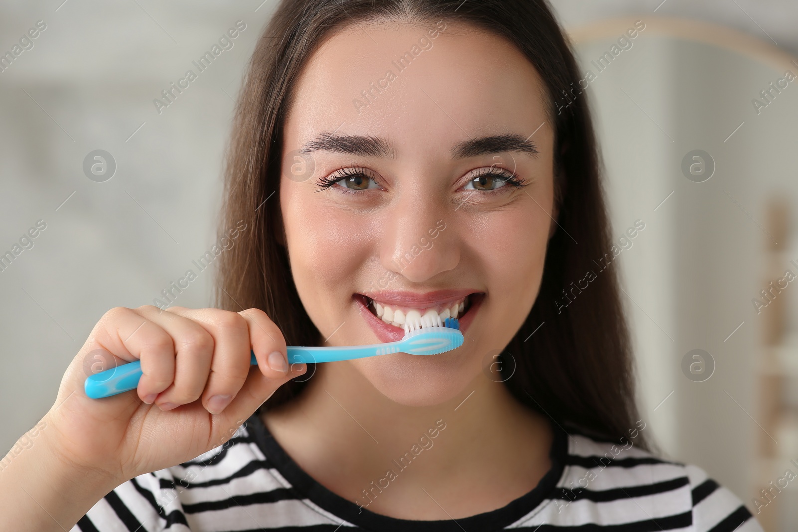 Photo of Young woman brushing her teeth with plastic toothbrush indoors, closeup