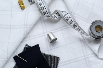 Photo of Silver thimble and other sewing accessories on checkered cloth, flat lay