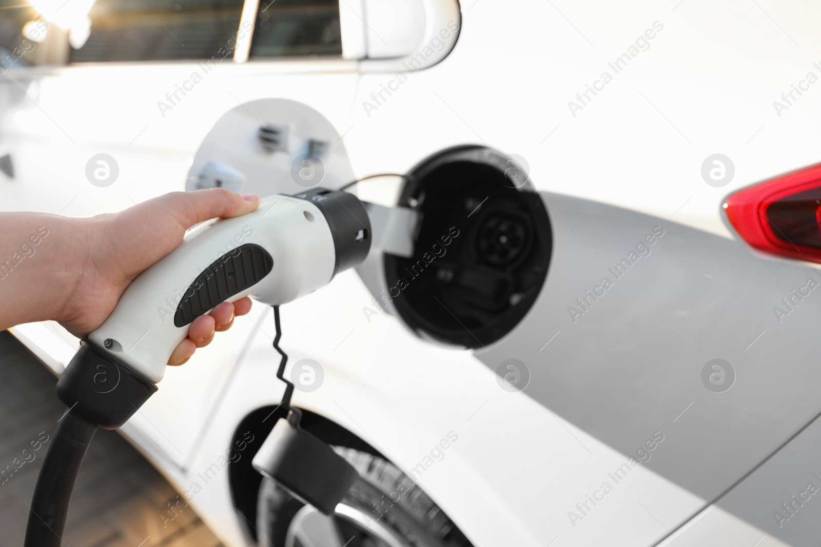 Photo of Woman inserting plug into electric car socket at charging station, closeup