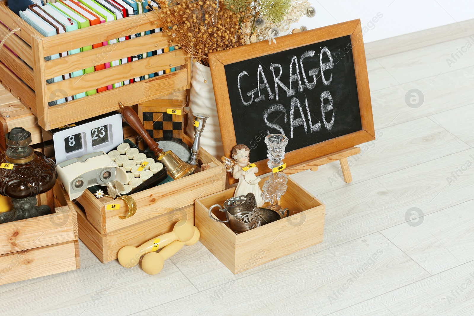 Photo of Sign Garage Sale written on blackboard near many different stuff on floor