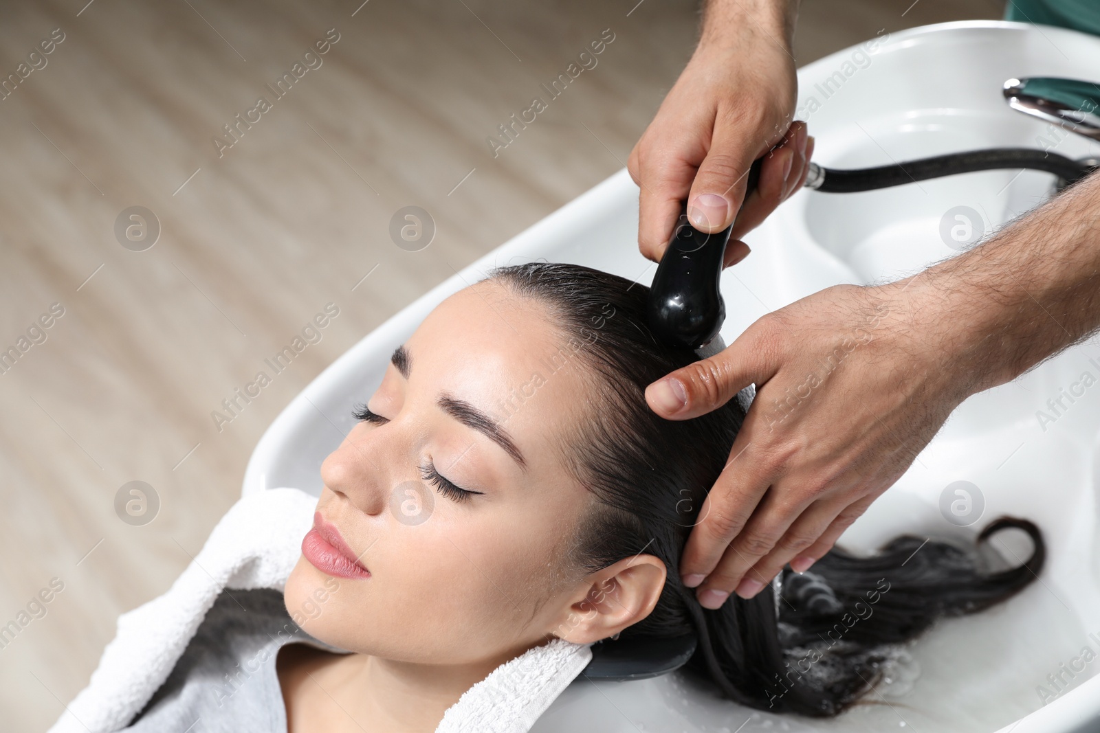 Photo of Stylist washing client's hair at sink in beauty salon. Space for text