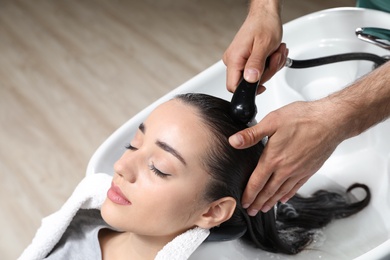 Stylist washing client's hair at sink in beauty salon. Space for text