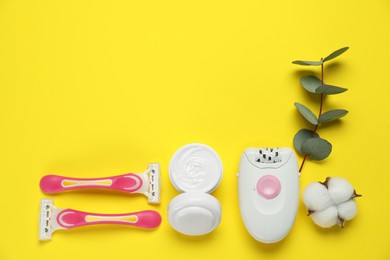 Modern epilator, razors, cream, fluffy cotton flower and eucalyptus branch on yellow background, flat lay. Space for text