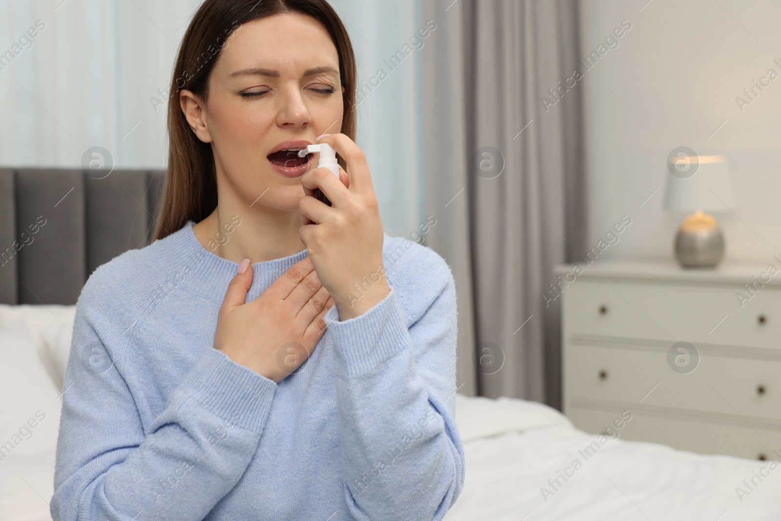 Photo of Adult woman using throat spray in bedroom, space for text