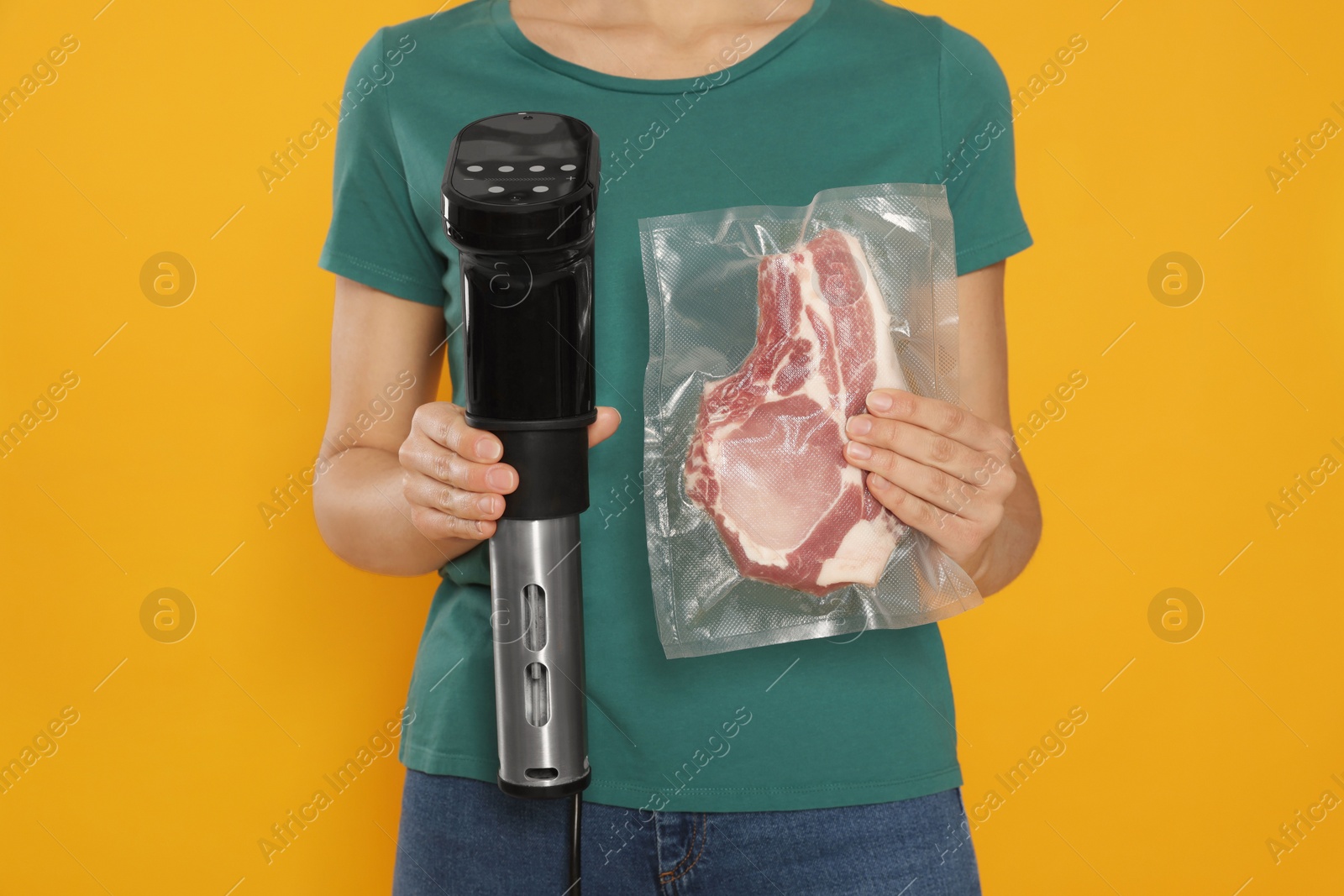 Photo of Woman holding sous vide cooker and meat in vacuum pack on orange background, closeup