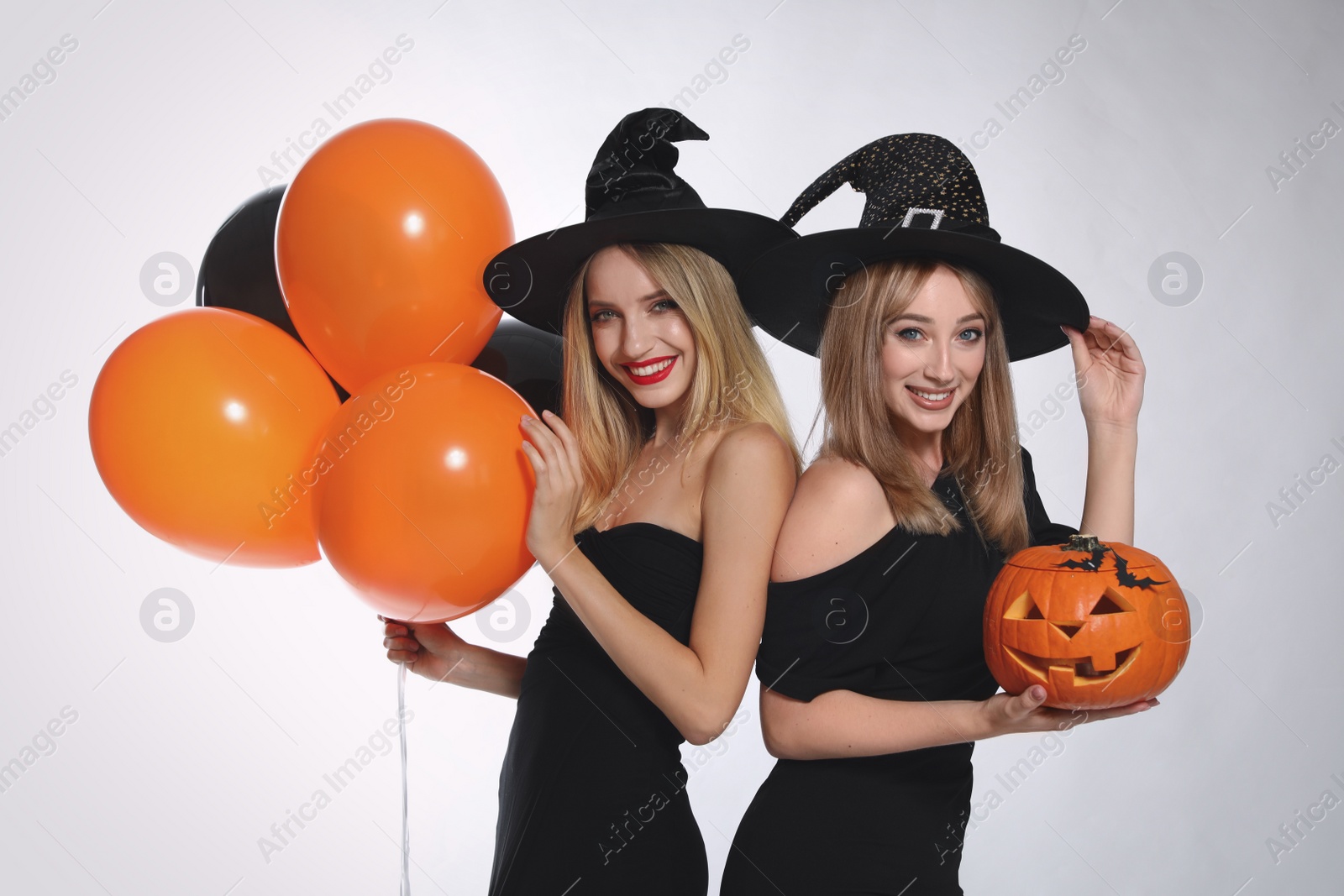 Photo of Beautiful women in witch costumes with balloons and jack o'lantern on white background. Halloween party