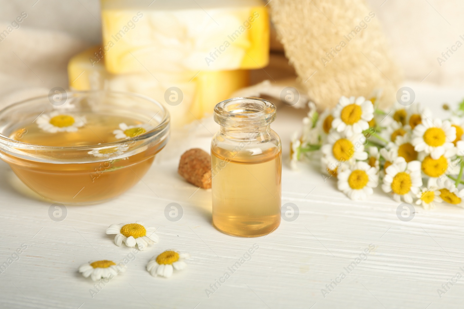 Photo of Essential oil and chamomiles on white wooden table