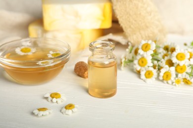 Essential oil and chamomiles on white wooden table