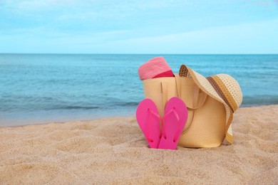 Summer bag with slippers, beach towel and straw hat on sand near sea, space for text