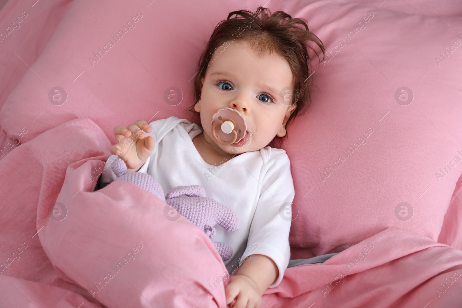 Photo of Cute little baby with pacifier and toy on bed, top view